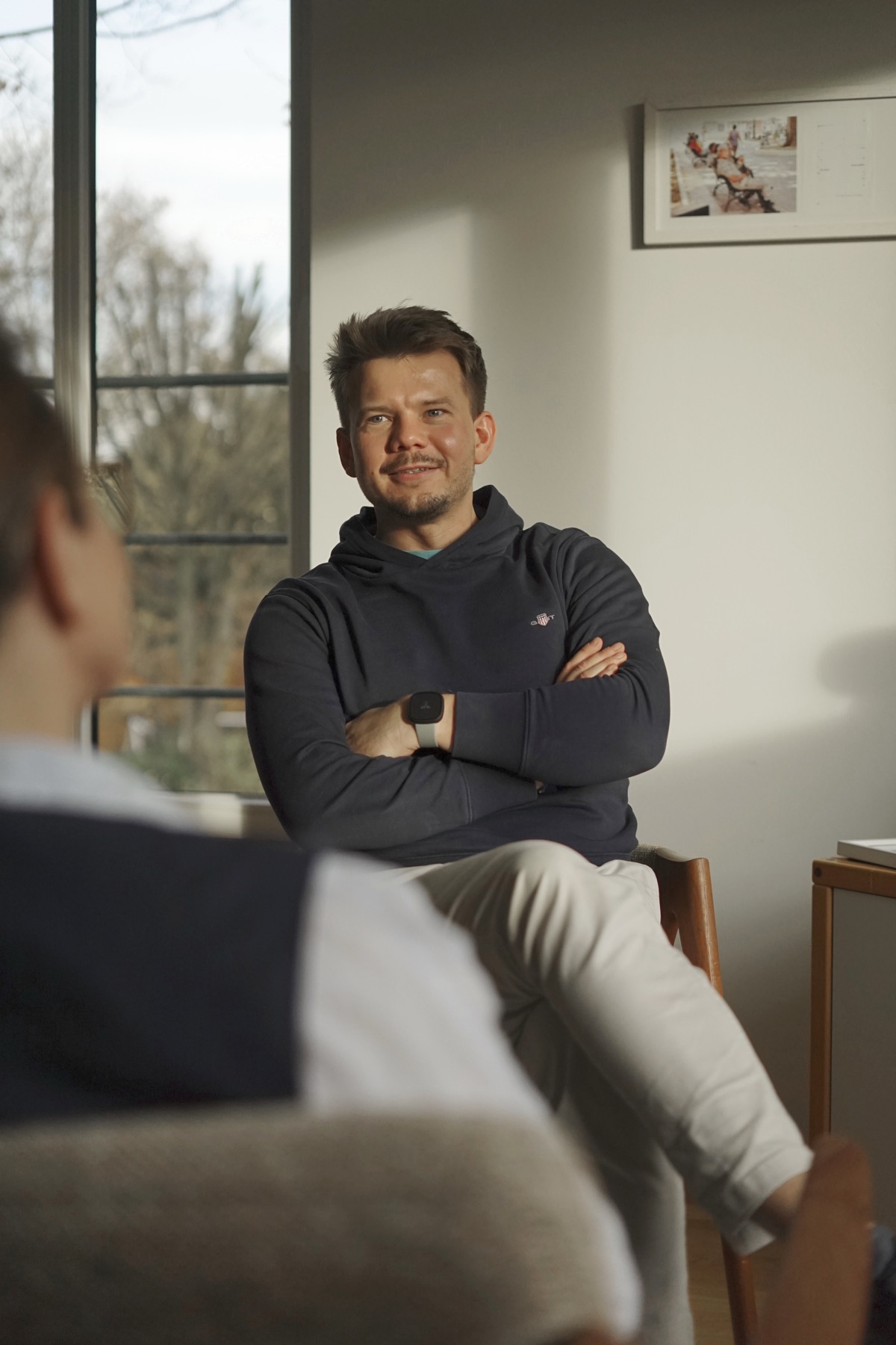 Ertmann Buchholz sitzt mit verschränkten Armen im warmen Fensterlicht